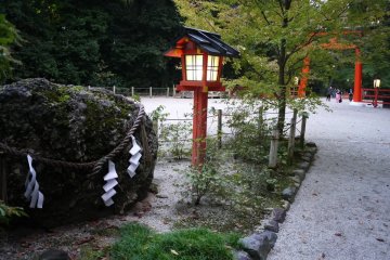 <p>Red wooden lantern stands beside a sacred rock</p>
