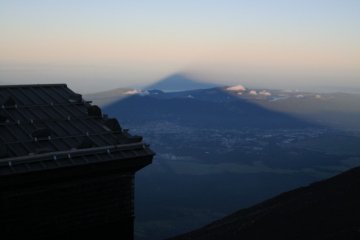 This is called Kage-Fuji, meaning Shadow of Mt.Fuji. This is a phenomenon where you see a shadow of Mr.Fuji appearing on the sea of clouds at the sunrise or the sunset.  