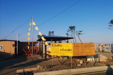 <p>An area where a house once stood now welcomes visitors in Arahama. You can view pictures of the town before and during the tsunami. Yellow flags can be found in some areas which express the desires of those that want to return.</p>