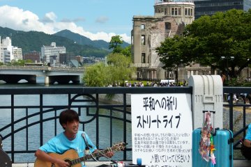<p>Museum playing on the bridge with view of A-bomb dome behind</p>