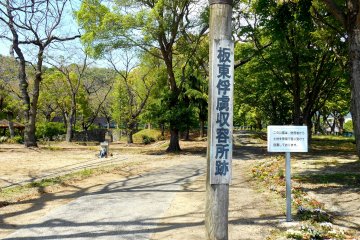 <p>Wooden board says, 'Bando POW Camp Site'</p>