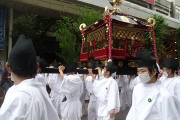 <p>Some priests carry a mikoshi, a means of transporting a Shinto deity and also a sort of portable shrine. White is a color of purity and the masks are to avoid polluting the air with their breath.</p>