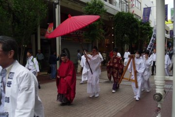 <p>A senior priest is protected from the elements by a wagasa, a type of umbrella.</p>