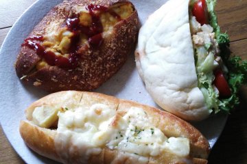 <p>Top left is a special curry bread with egg and tomato sauce; to the right is a "pizza pita" with lettuce, tomato, egg and a creamy sesame dressing; and below is a bun filled with potato salad and covered in cheese.</p>