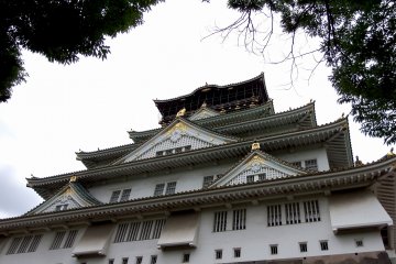 Sekarang Anda berdiri di depan menara utama Kastil Osaka, tetapi Anda baru saja masuk dari pintu belakang dan ini adalah pemandangan samping kastil. Anda harus berkeliling untuk sampai ke depan kastil...