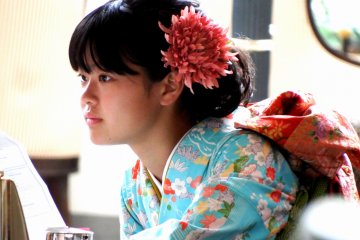 <p>Lovely flower decorating her hair goes well with the blue color of her kimono and matches the color of the Obi sash. Perfect!</p>