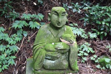 <p>A stone figure with a baby deer in his arms</p>