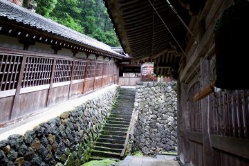 Small bell hanging from the eaves of Buddha Hall. The covered wooden building on the left is the long stairs that connect buildings