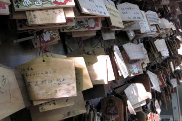 <p>These wooden prayer plaques, known as ema, are used by Shinto worshippers to record their prayers or desired wishes. All of the plaques have maneki neko designs painted on them in respect to the maneki neko&nbsp;shrine directly behind it.</p>