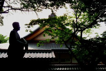 <p>Statue of Matsuo Basho, the Japanese famous poet, dark trees and the glimpse of gold ornaments of one of the shrine buildings</p>