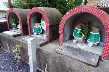 <p>Three pairs of jizo statues stand in a corner of the temple grounds</p>