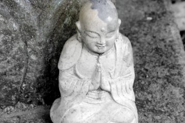 <p>A small Jizo statue sitting silently at the foot of one of the Kannon Bosatsu statues</p>