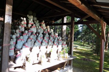 <p>Another group of small jizo statues under a wooden hut on the temple grounds</p>