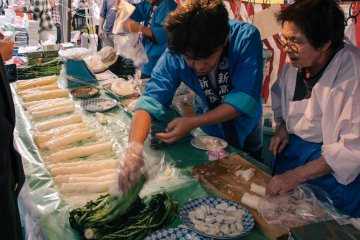<p>A vendor getting Nozawa for a customer while his mother is chopping pickled daikon radishes for other customers to taste.&nbsp;</p>