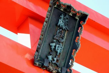 <p>Deep green signage of Fujishima Shrine hanging on the red torii gate</p>