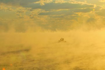 A fishing boat fades in and out of view in a sea of cloud