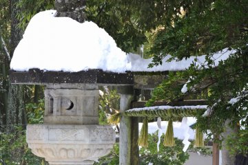 <p>Stone torii gate leading to the pilgrimage pathway to the Thirty-Three Kannon Statues, with a snow-capped stone lantern in the foreground</p>