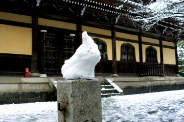 <p>A snow bunny sitting on a marker post in front of the temple</p>
