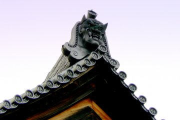 <p>A gargoyle with a damaged face on a roof apex</p>