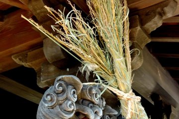 <p>A mythical shishi peeking around the end of a straw rope</p>