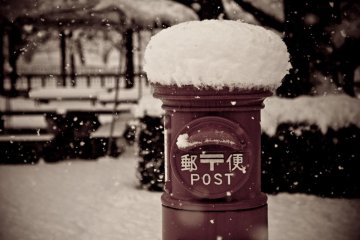A traditional-style postal box sits beneath a thick layer of snow in the Edo Tokyo Museum.