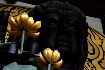 <p>Echizen Daibutsu statue sitting with golden lotus flowers in hand</p>