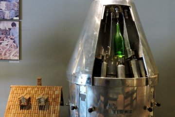<p>A house made of corks stands next to something that looks a bit like a rocket's landing pod. &nbsp;</p>