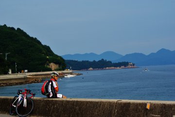 <p>Un cycliste se repose pr&egrave;s d'une plage de Mukaishima</p>