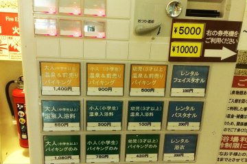 <p>The machine to buy your ticket. The top row of yellow buttons are tickets for both the entrance into the hot spring and lunch buffet. Starting from left to right is the price for adults (￥1,400), elementary age kids (￥900)&nbsp;and young children over the age of 3 (￥500). The middle row of blue buttons is entrance into the hot spring only, and the bottom row of green buttons is for the buffet only. &nbsp;The row of blue buttons on the right side is for rentals. The top one is face towel rental (￥100), the middle is bath towel (￥200), and the bottom is for a Japanese robe (￥200)</p>