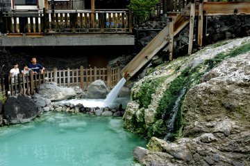 <p>Tourists watch water fall into a pool at the lower end of Yubatake</p>
