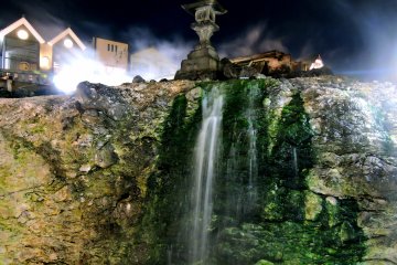 <p>A stone lantern stands at the top of a steaming waterfall</p>