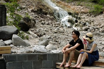 Des visiteurs sont assis au bord d'un bassin, devant une cascade d'eau chaude