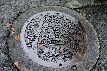 Akasawa-juku's manhole cover features cherry blossoms and another spring flower