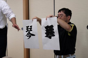 <p>The leader of the sumo calligraphy workshop demonstrates the difference between regular calligraphy (produced by holding the brush at a 90 degree angle) and sumo calligraphy (produced by using lots of ink and holding the brush at a 45 degree angle). The thick, heavy brush strokes of the sumo style calligraphy is indicative of a sumo's power and strength</p>