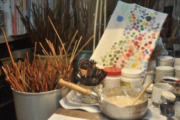 <p>Wooden sticks, used to frame up a piece of cloth, glue and paintbrushes are readily available on the table.</p>