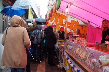 <p>Huddled in raincoats and under umbrellas, locals wait in line for delicious street food.</p>
