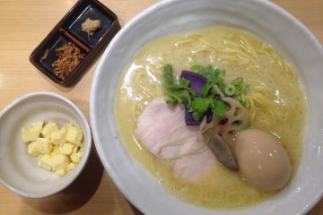 <p>Lihatlah kuah sup kaldu ayam yang kental, <i>creamy</i>, dan mengkilap ini. Terdapat hiasan sayuran hijau dan ubi biru, ditambah ajitsuka tamago, dan irisan ayam yang renyah namun meleleh di mulut. Terlihat juga&nbsp;<em>butter garlic</em>&nbsp;dan bawang goreng.</p>
