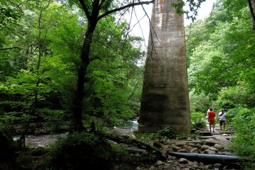 Tall pylons of a rail bridge across the stream tower over sightseers walking the trail