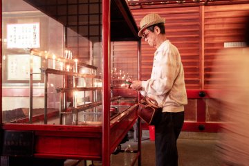 Seorang pria menyalakan lilin di dalam Aula Ichigandou