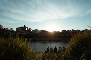 A group of friends take time off, eating and drinking while they sit on the riverbank
