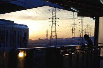 In the early morning, a boy reads a magazine while waiting to catch his train at Kōshū-Kaidō station