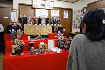 A young lady sits eagerly while her portrait is drawn by a humorous painter puppet