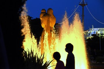 Silhouettes of a couple walking behind the statue of the Goddess of Water