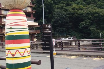 An aging kokeshi guards the bridge crossing the river