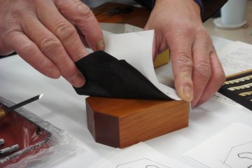 First fit a copy of your chosen character and a piece of carbon paper on the wooden shogi piece- Tendo Town, home of Japanese chess