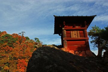 The autumnal trees in the distance complement the red of this small shrine.
