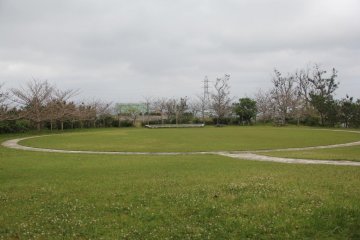 An open air gathering area in the native village area on the grounds of the Zakimi Castle Ruins.  A stage can be seen in front of the grassy viewing area.