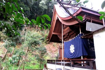 The shrine is set in a mature garden with a backdrop of verdant hills and bamboo groves
