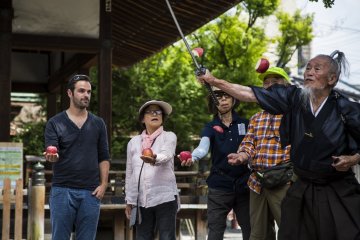 Okada systematically throws up apples held by volunteers and slices the fruits in the air