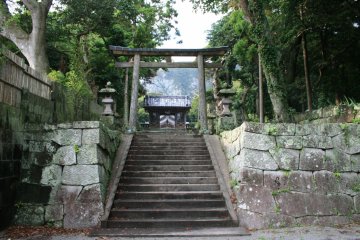 <p>green mountains behind old wooden entrance to Jusansha Shrine</p>